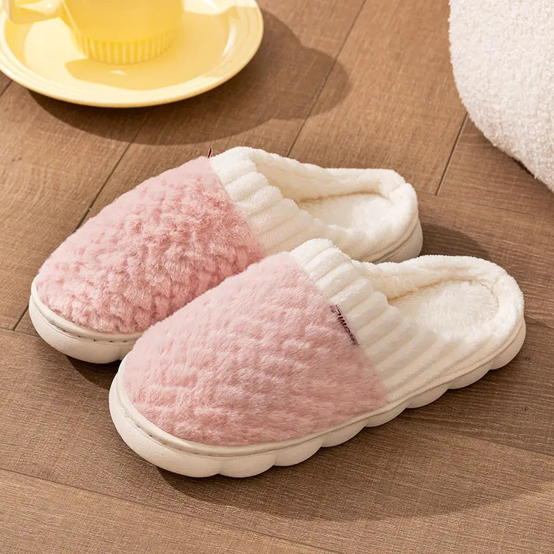 A pair of pink and white plush fleece slippers resting on a wooden floor next to a yellow plate.