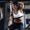 A smiling woman performing a physical exercise with kinesiology tape on her arm in a gym setting.