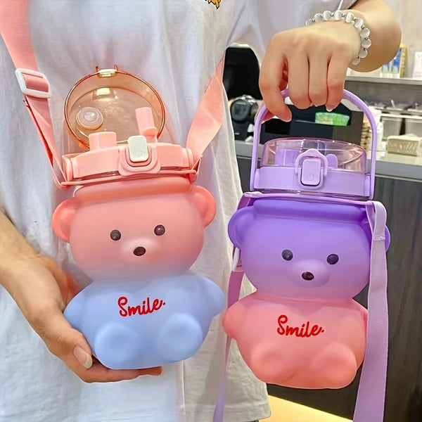 A pink bear-shaped portable water bottle with a straw and strap is held in a person's hand.