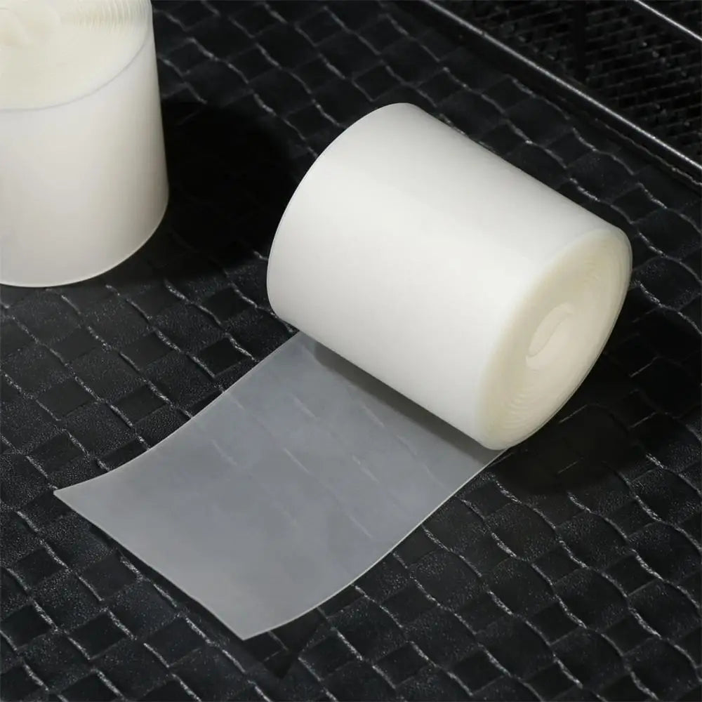 Un rollo de forro para llanta de bicicleta transparente junto a un contenedor blanco sobre una superficie negra texturizada.