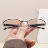 A hand holds a pair of retro oval sunglasses with a silver metal frame against a light background.