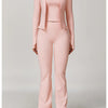 A woman models a three-piece pink yoga sports set consisting of a long-sleeved jacket, cropped top, and matching pants.