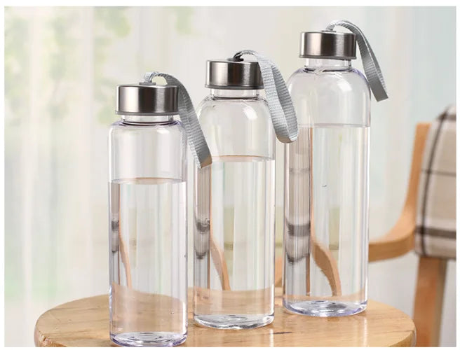 Tres botellas de agua de vidrio transparente con tapas de silicona gris sobre una superficie de madera.