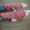 Pair of pink crocodile knit socks with grey cuff resting on a wooden surface.