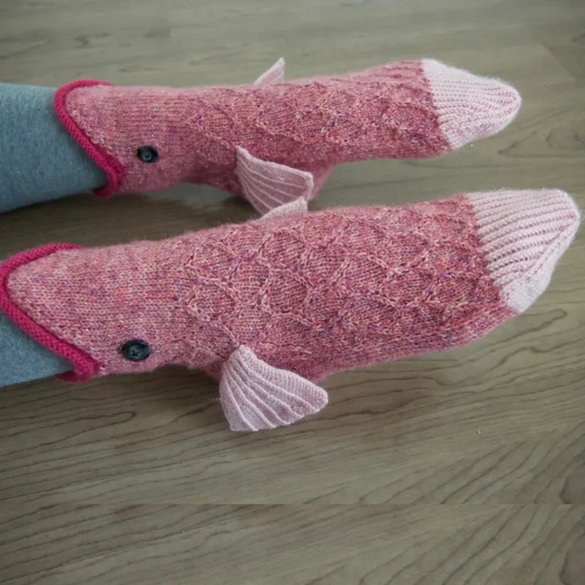 Pair of pink crocodile knit socks with grey cuff resting on a wooden surface.