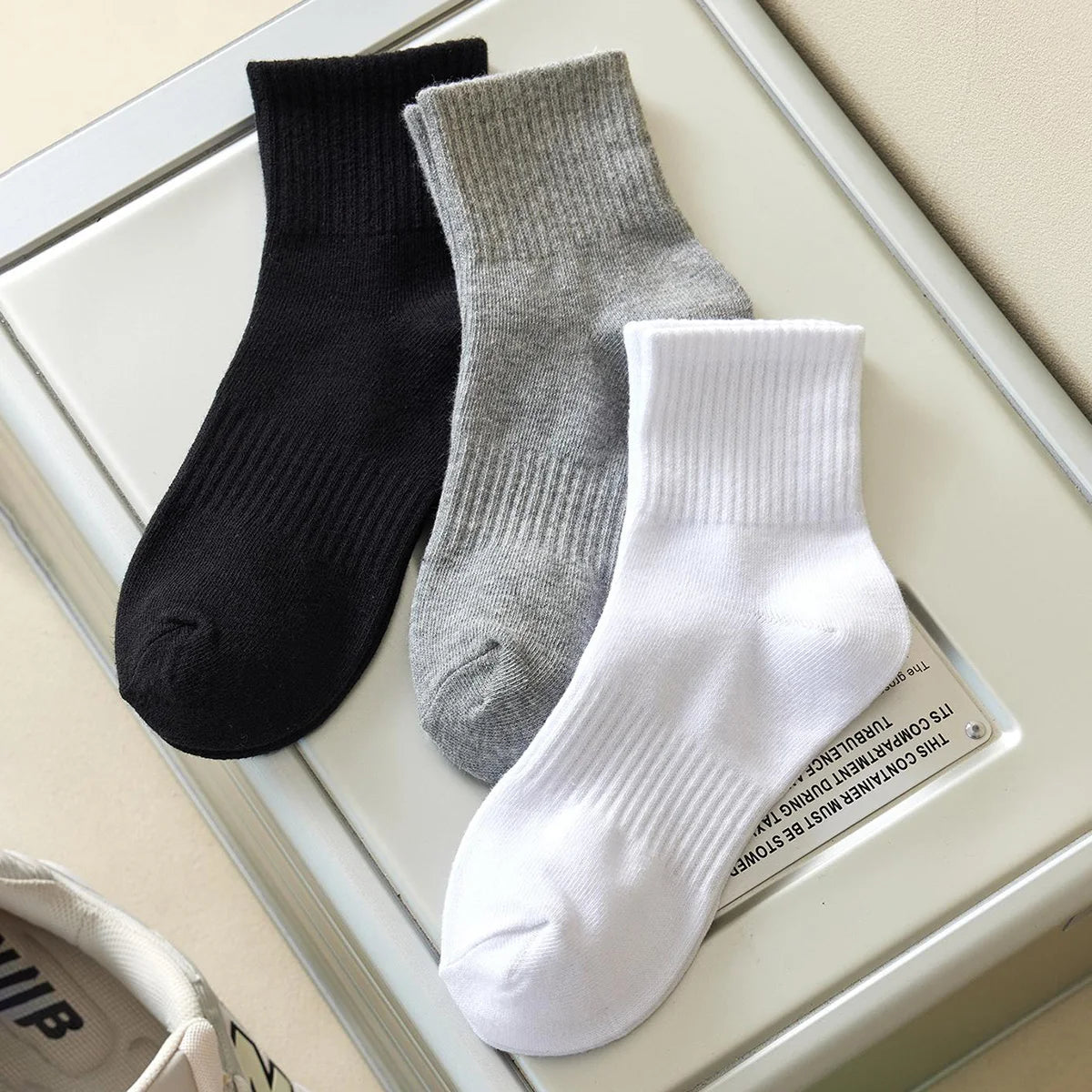 A set of three crew socks in black, gray, and white displayed on a white tray.