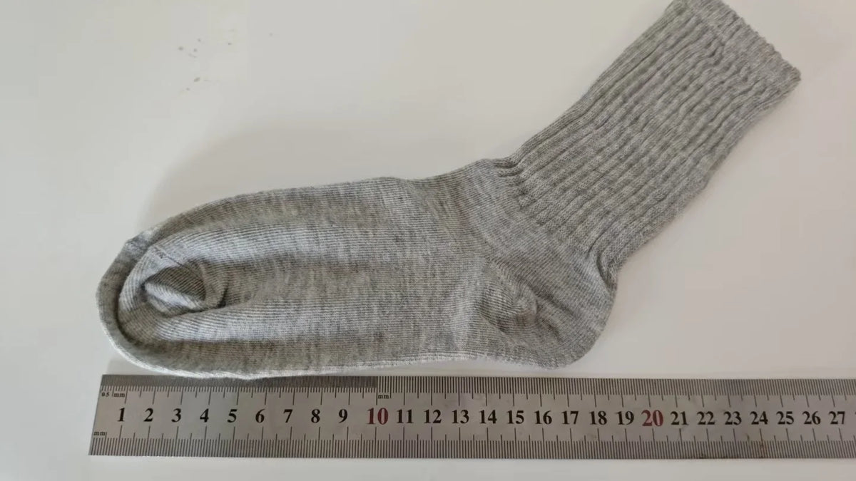 Calcetines de punto grises mostrados planos junto a una regla que muestra su longitud.