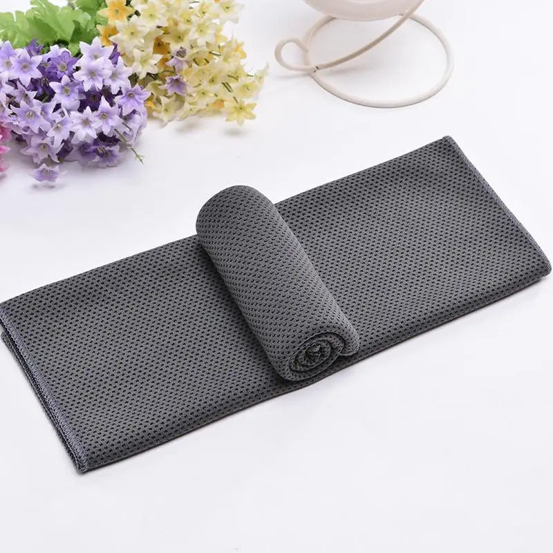 Serviette de refroidissement grise foncée en forme de cercle roulée sur une surface blanche avec des fleurs jaunes claires en