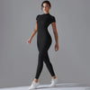 A model wearing a black Naked Zipper Yoga Jumpsuit standing against a gray background.
