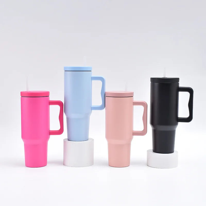 Trois tasses isothermes en acier inoxydable rose, bleu et noir avec des bases blanches.