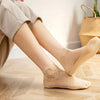 A person wearing beige lace mesh ankle socks while sitting on a wooden floor.
