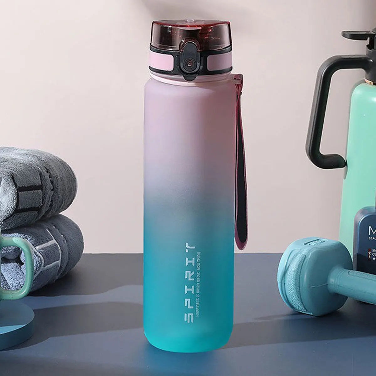 Eine hohe, gradientblaue Wasserflasche neben einer grünen Gym-Flasche und einem Set grau-grüner Trainingshandtücher.