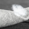 Gros plan d'une main portant une chaussette tricotée gris clair avec des fibres blanches visibles au col.