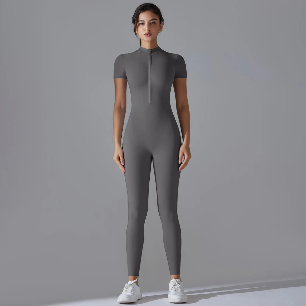 A model wearing a full-body, long-sleeved gray yoga jumpsuit with a high neck zipper.