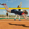A female athlete performing a dive or stretch over a tennis net during outdoor practice.