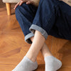 A person is sitting on a wooden floor wearing dark blue jeans and light beige shirt, with gray ankle socks visible.