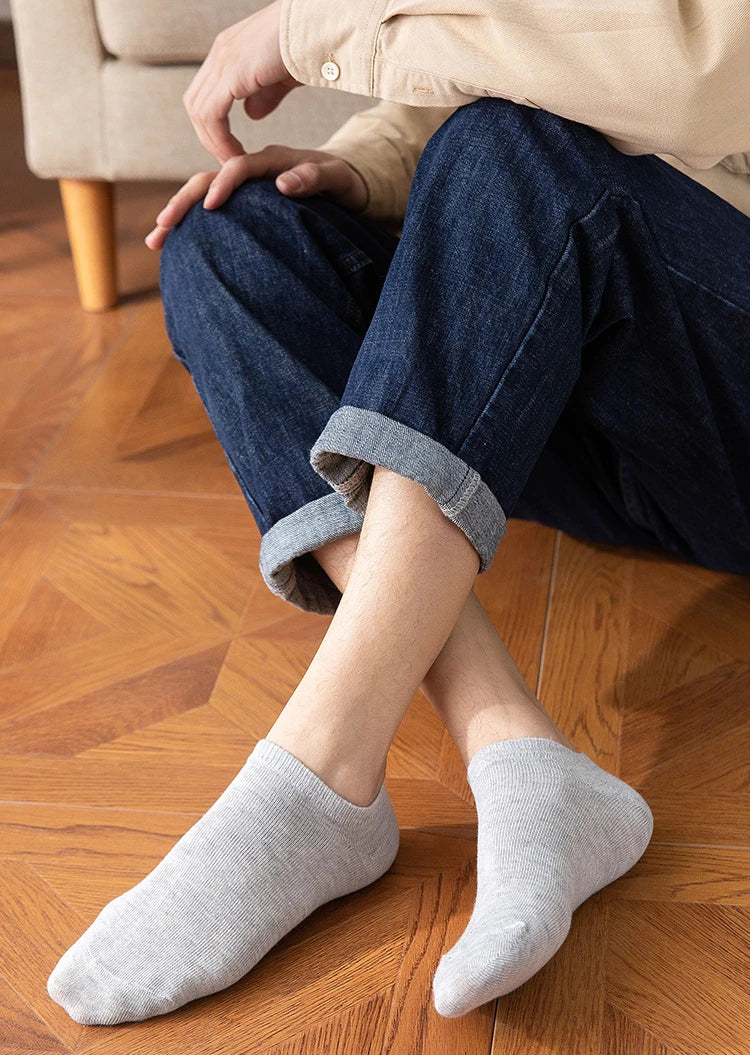 A person is sitting on a wooden floor wearing dark blue jeans and light beige shirt, with gray ankle socks visible.