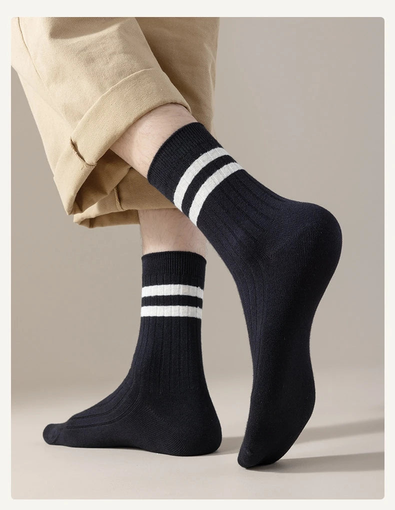A close-up of black striped men's socks worn on a foot, paired with light tan trousers.