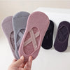 Una mano sostiene un par de calcetines de yoga y pilates de color rosa y gris sobre una superficie blanca.