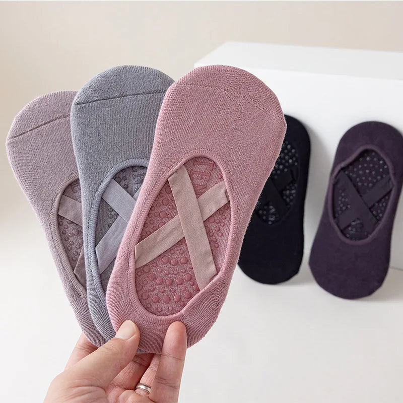 Una mano sostiene un par de calcetines de yoga y pilates de color rosa y gris sobre una superficie blanca.