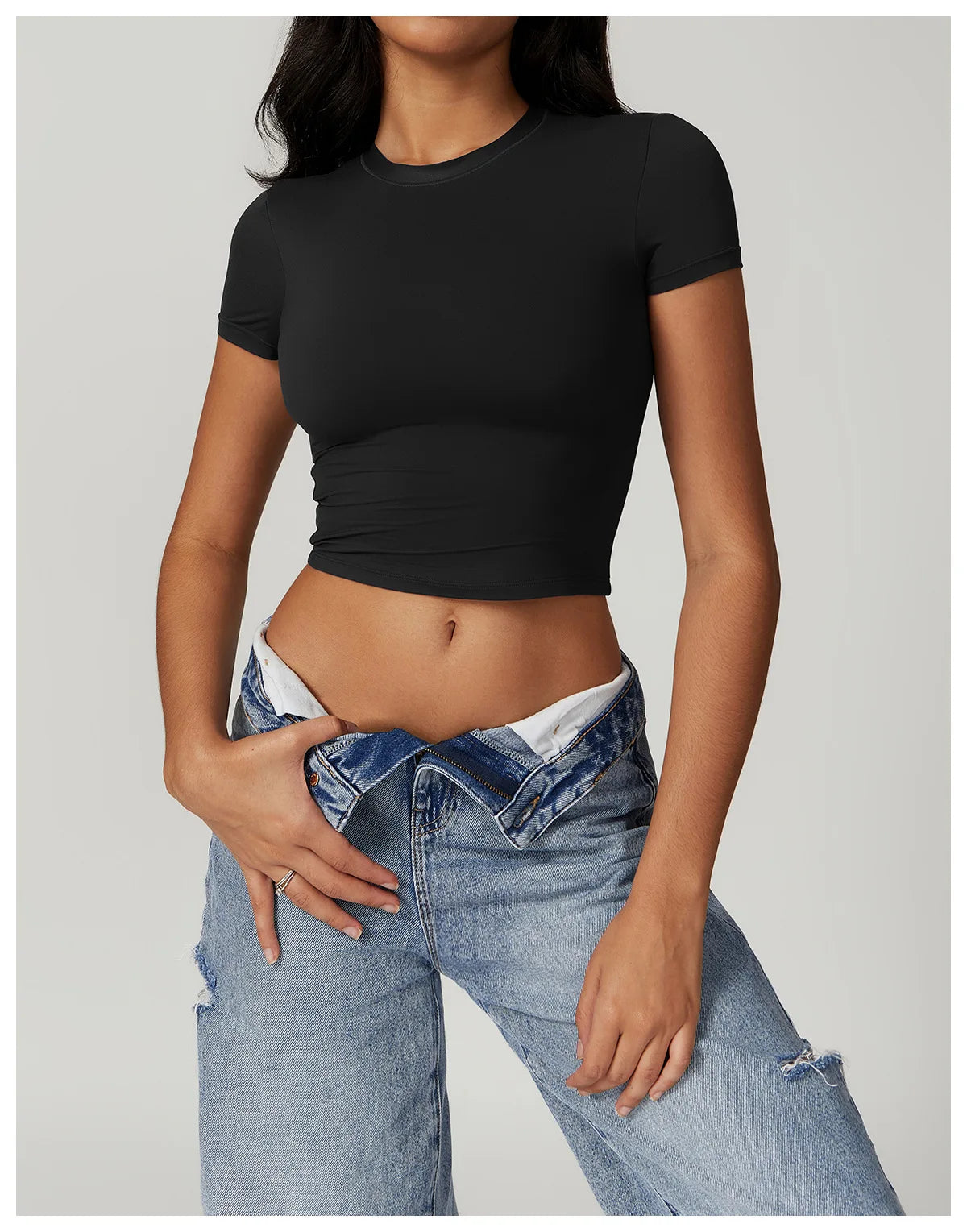 Una mujer vistiendo una camiseta negra de yoga y fitness de secado rápido y jeans azules.