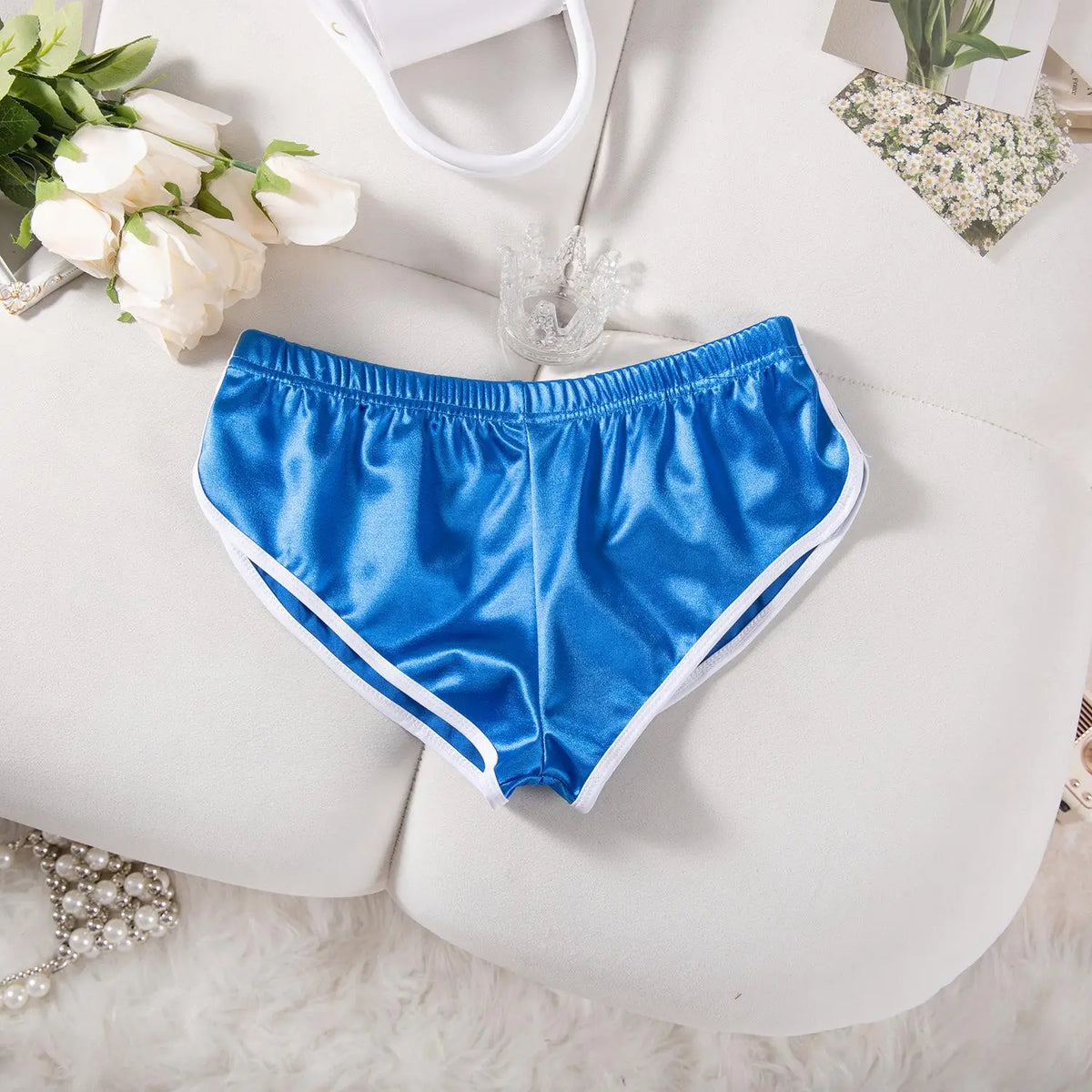 Helle blaue Satin-Jogginghose, flach auf weißer Oberfläche mit Blumenakzenten.