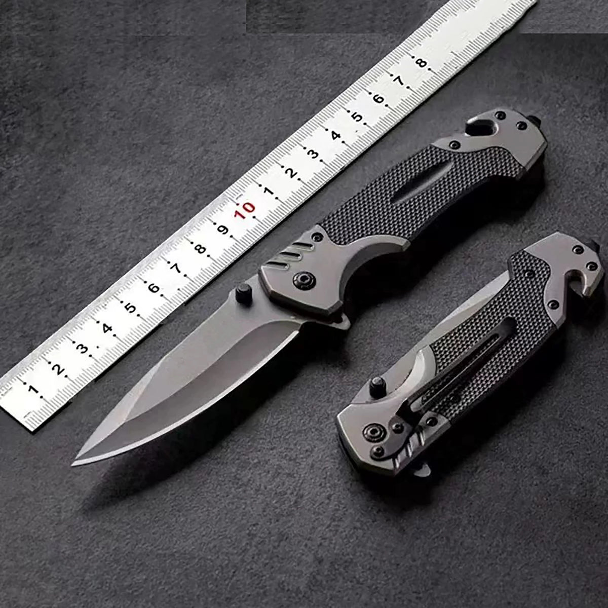 A multi-functional folding survival knife is shown next to a ruler on a dark surface.