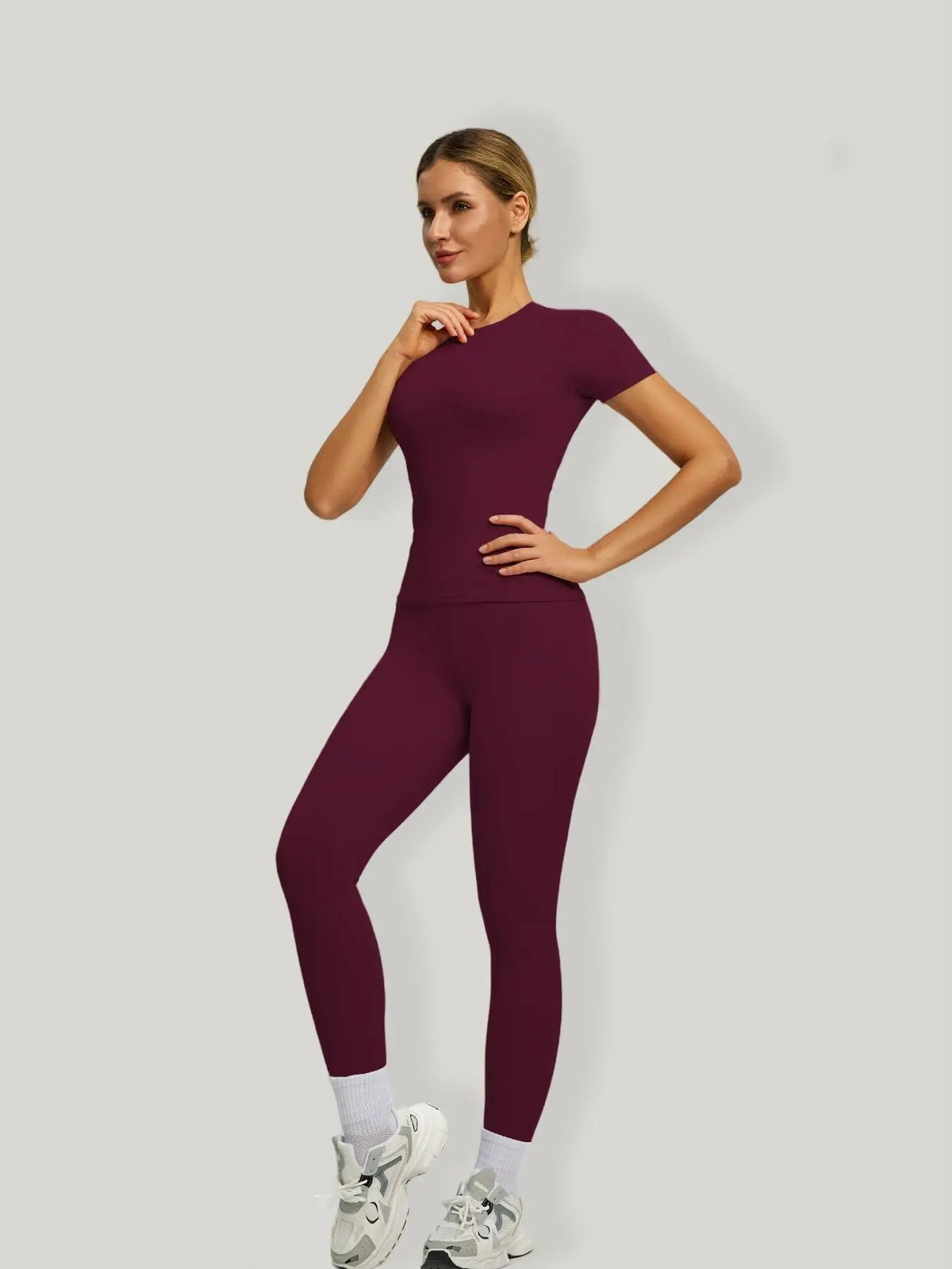 Eine Frau modelliert ein sportliches Yoga-Set in tiefem Bordeauxrot mit kurzem Oberteil und Leggings.