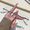 A hand holds a pair of frameless rectangle blue light blocking glasses with silver detailing.