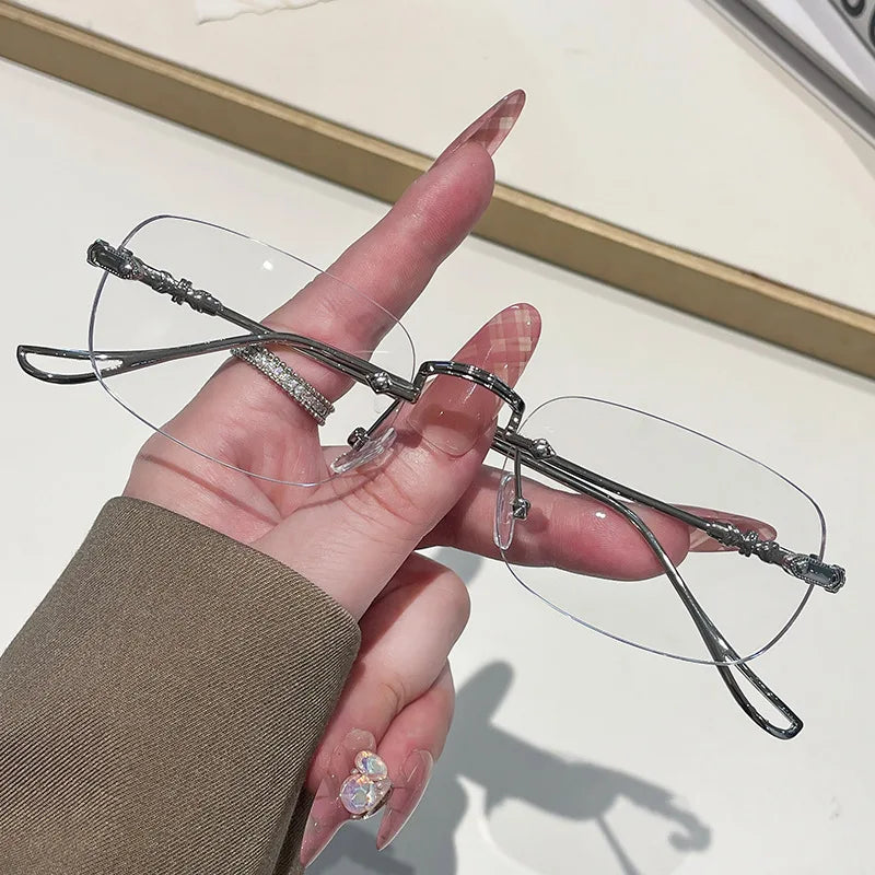 A hand holds a pair of frameless rectangle blue light blocking glasses with silver detailing.
