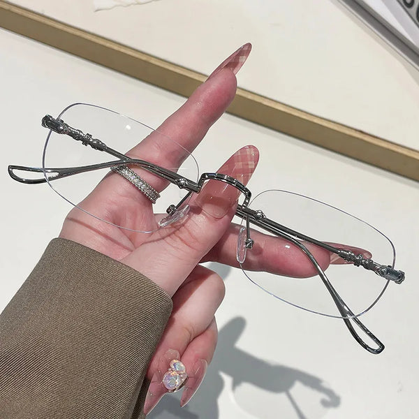 A hand holds a pair of frameless rectangle blue light blocking glasses with silver detailing.