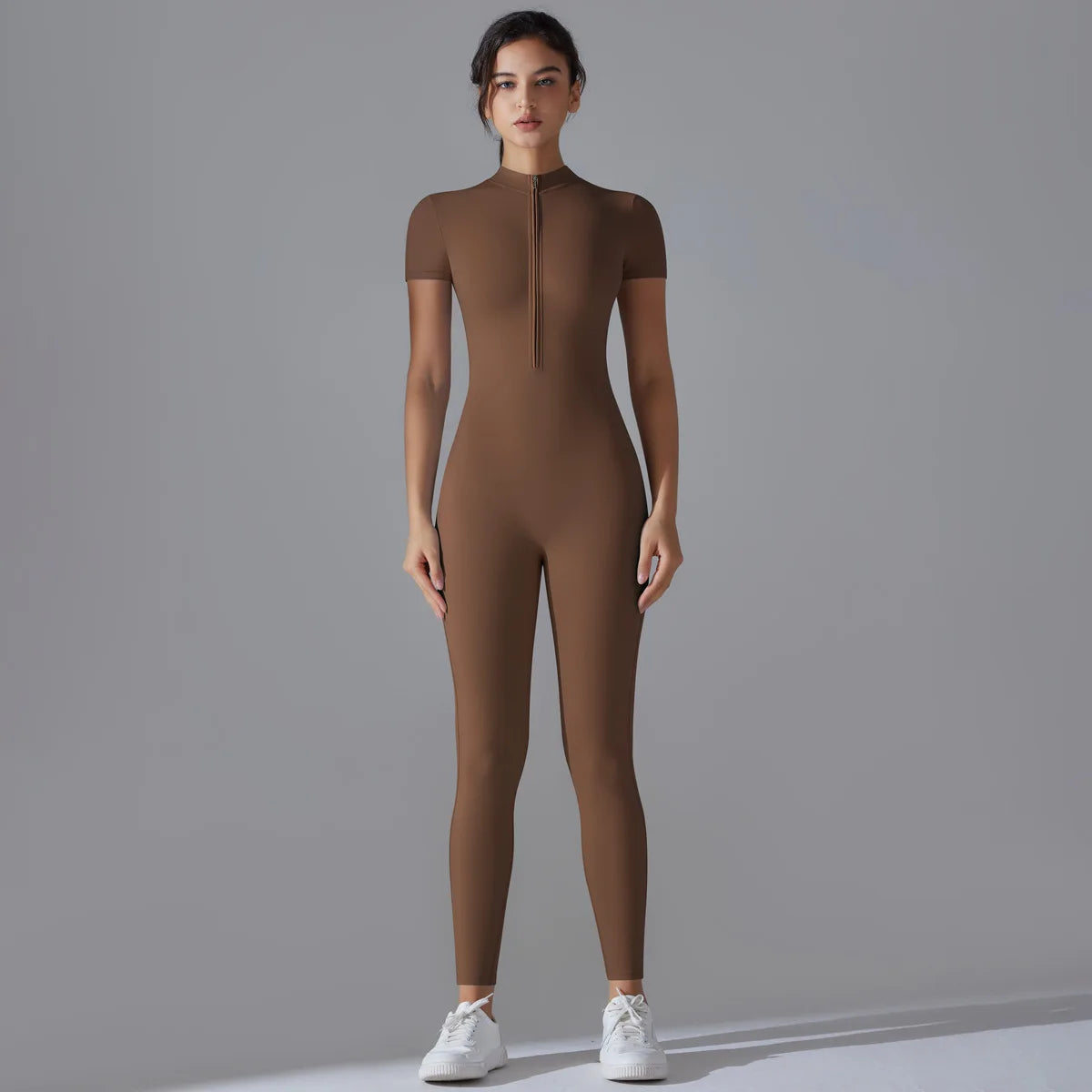A model wearing a full-body, long-sleeved brown yoga jumpsuit with a high neck zipper.