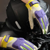 A close-up of yellow and purple breathable motorcycle riding gloves being worn on a hand.
