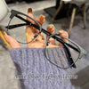 A hand holds a pair of black retro square blue light blocking eyeglasses against a gray knitted sweater.