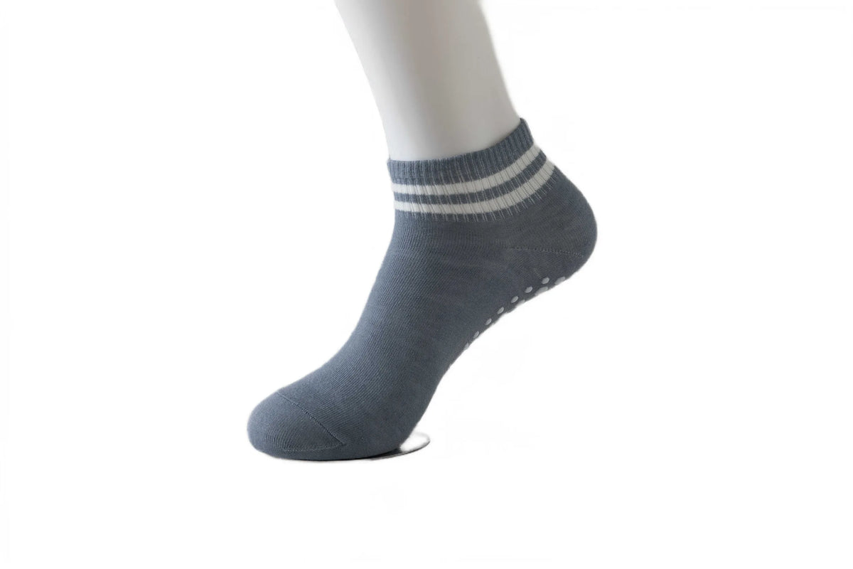 Gray non-slip grip socks with a ribbed cuff and white stripes worn on a model's foot.