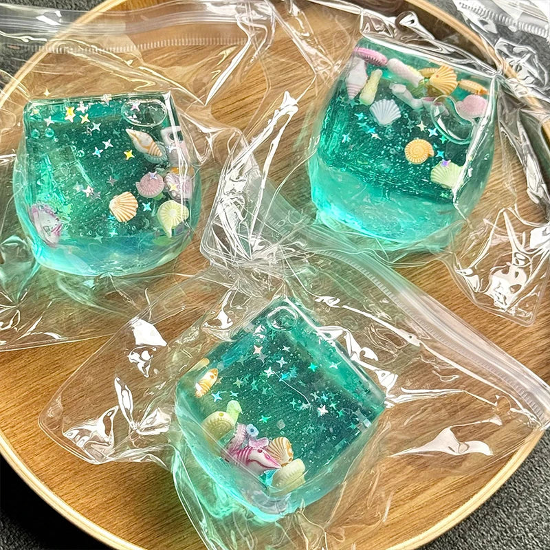 A collection of teal and green squishy stress relief fidget cubes with glitter and sea life designs packaged in clear plastic