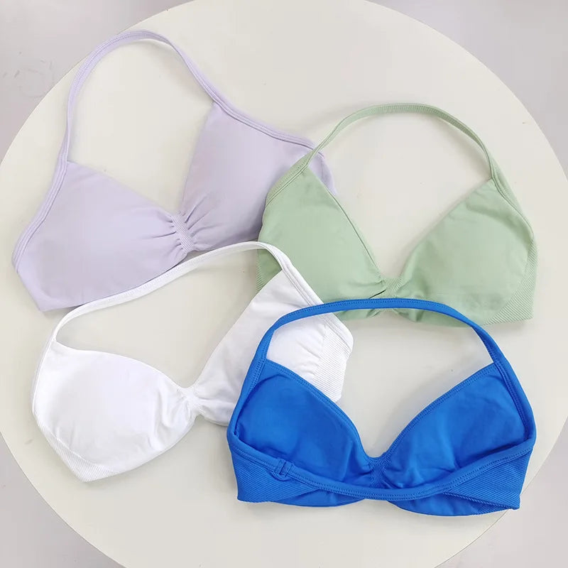 Una colección de cuatro sujetadores deportivos de encaje con cordones en lavanda, verde claro, blanco y azul real.
