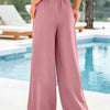 A model is wearing dusty rose flowy high waist drawstring wide leg pants outdoors near a swimming pool.