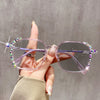 A hand holds a pair of pink photochromic diamond style eyeglasses with iridescent accents against a gray background.