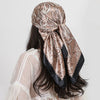 A woman wearing a silk paisley shawl scarf with gold and black patterns, shown from the back.