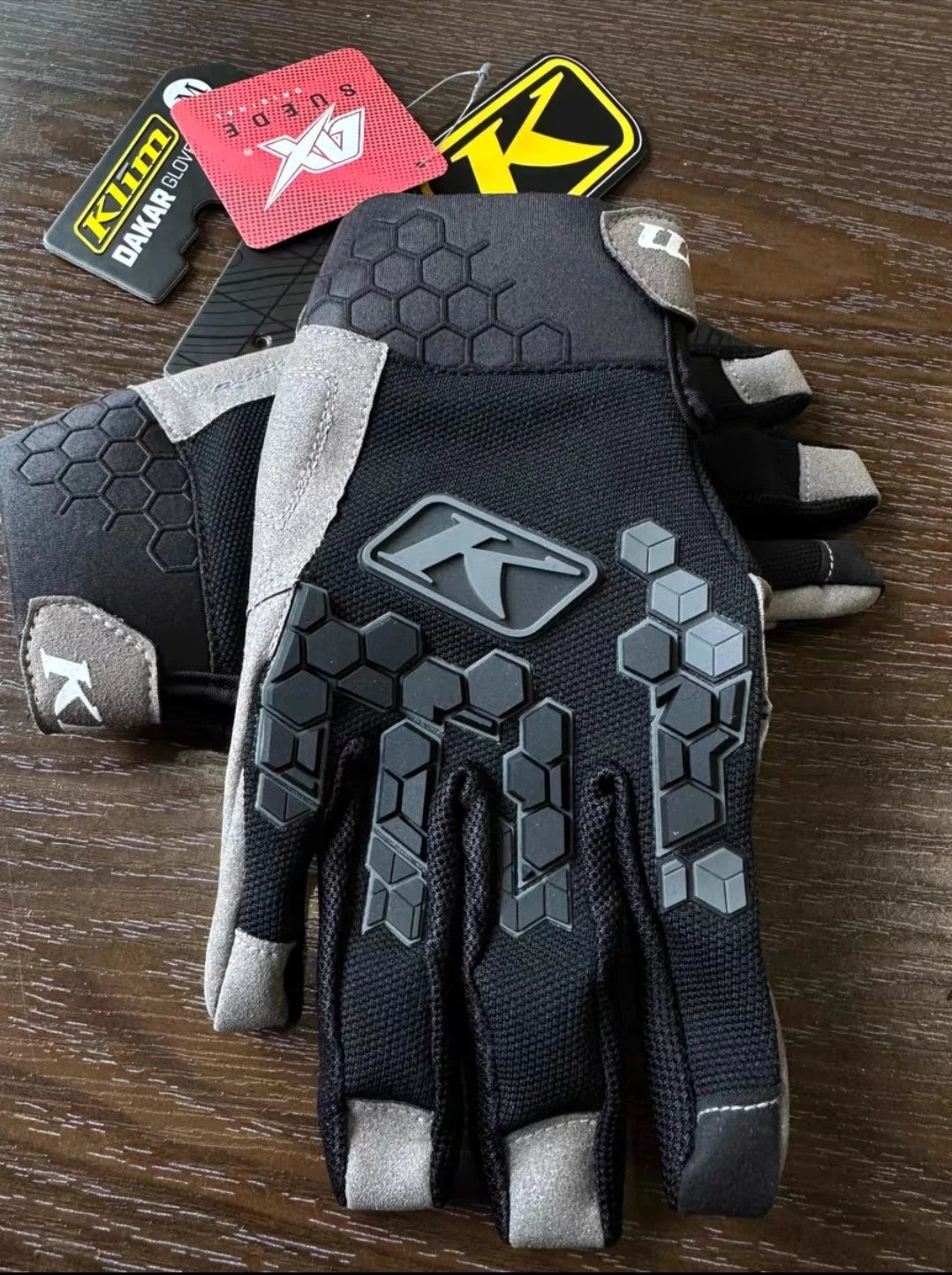 Une paire de gants de moto tactiques noirs avec des accents gris et une texture de prise sont présentés sur une surface en bo