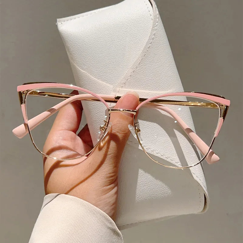 A hand holds a pair of pink cat-eye blue light blocking glasses resting on a white leather case.