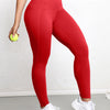 A woman wearing red high-waisted sports leggings and a cropped top stands while holding a lime green ball.