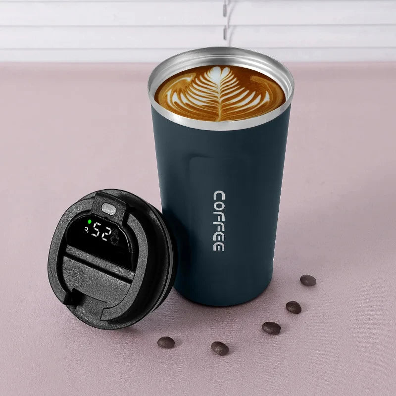 A dark blue insulated thermos bottle with a lid and a latte art coffee drink inside, resting on a pink surface.