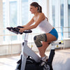 A woman is exercising on a stationary bike while wearing a copper ion knee support sleeve.