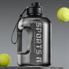 Klare Sportflasche mit schwarzem Verschluss und Drahtschlaufe neben einem Tennisball.