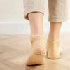 A pair of beige lace mesh ankle socks being worn by a person standing on a wooden floor.