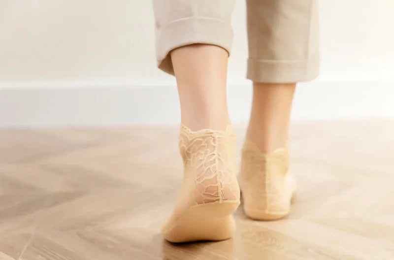A pair of beige lace mesh ankle socks being worn by a person standing on a wooden floor.