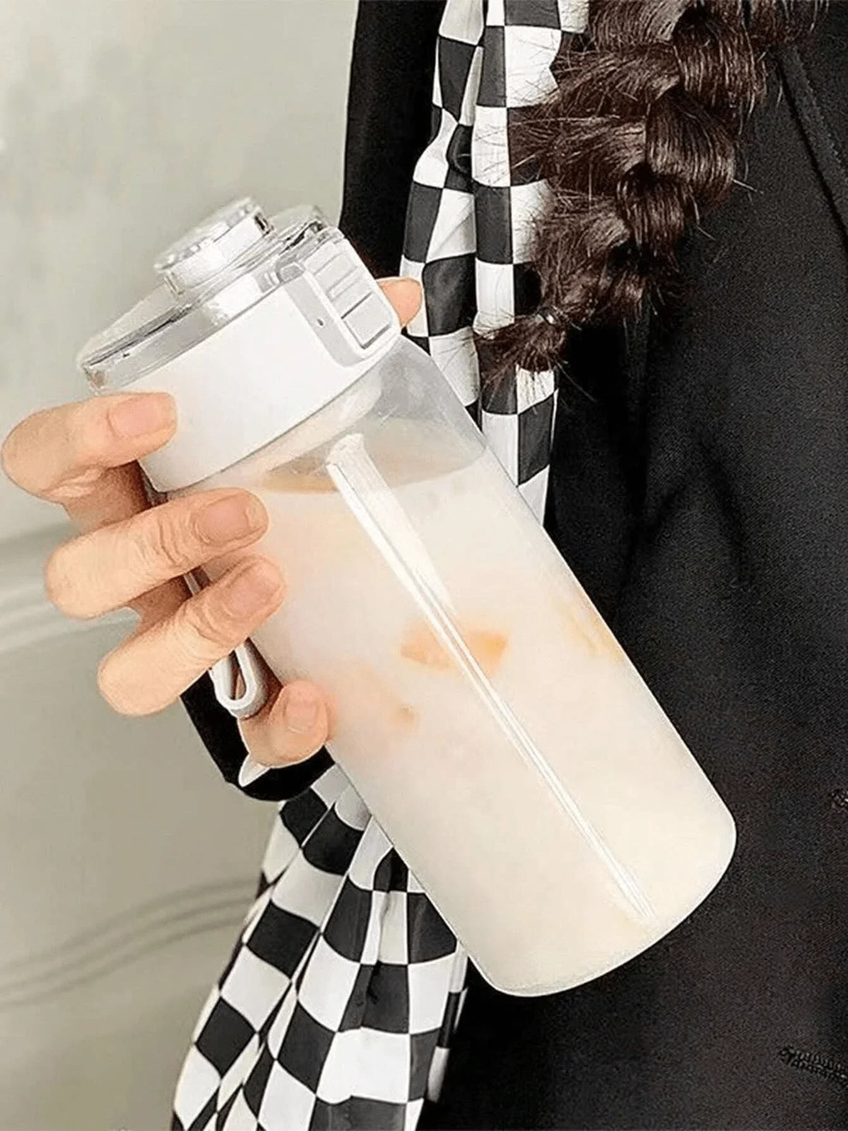 A hand holds a large capacity transparent sports water bottle filled with a milky liquid.