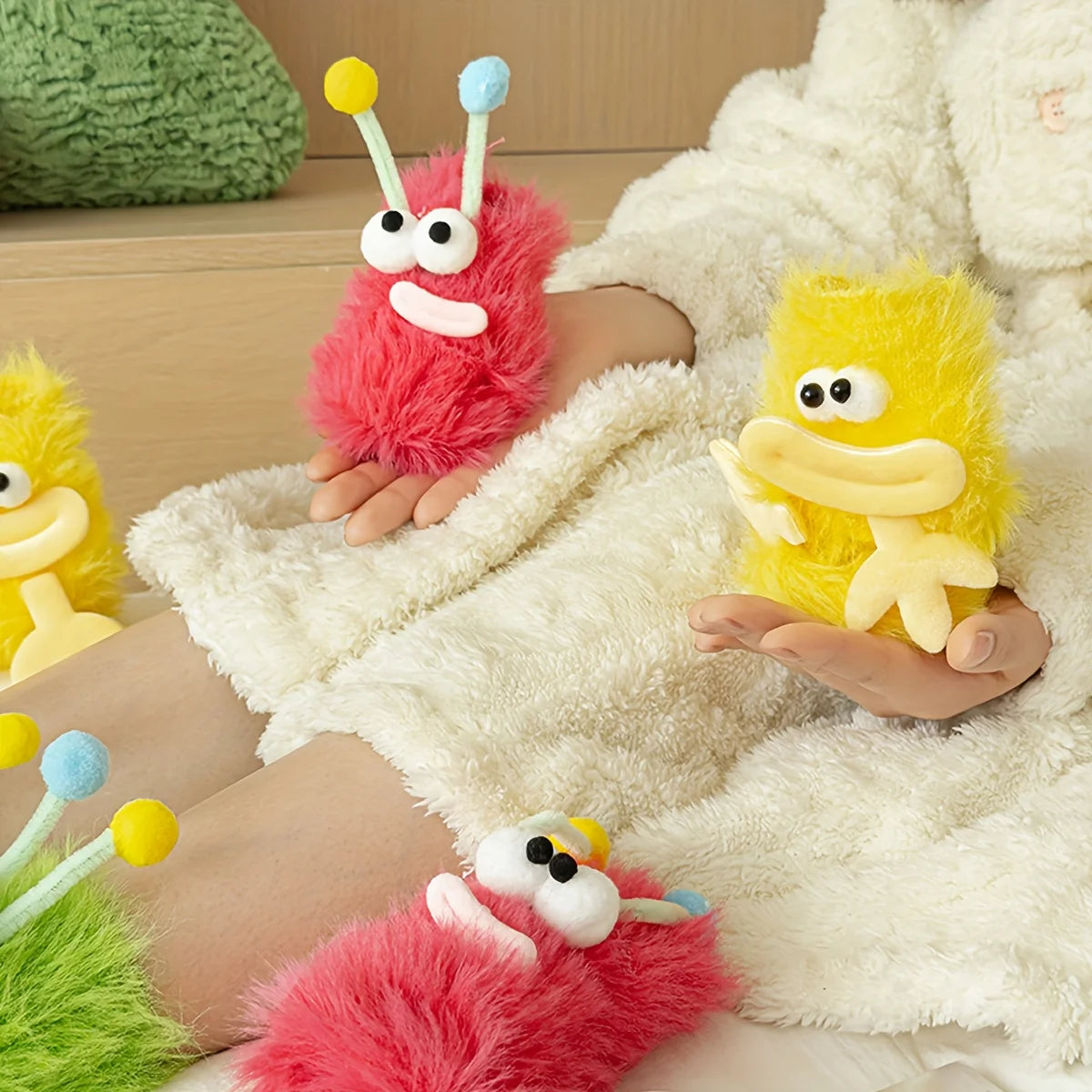 A collection of funny plush caterpillar floor socks in pink, yellow, and white are displayed on a cream-colored blanket.